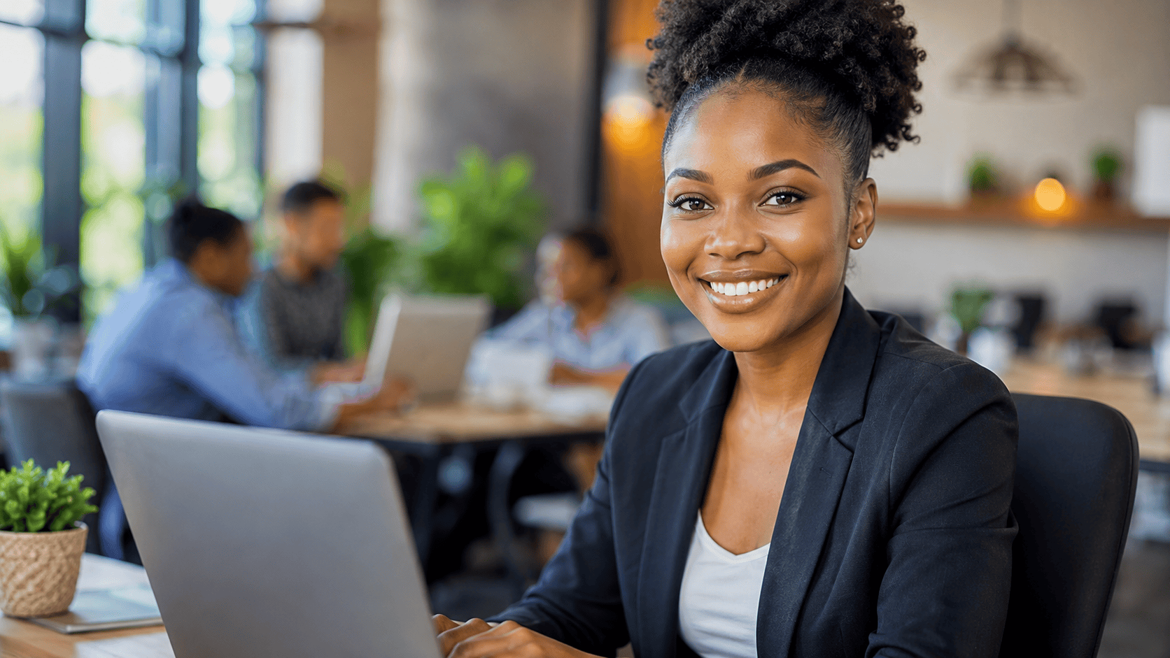 A confident young Nigerian female graduate smiling while working on a laptop in a modern office space, with blurred coworkers in the background, representing entry level job opportunities for fresh graduates in Nigeria in 2026.
